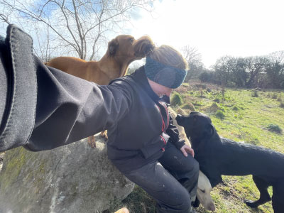 Jenny sat on a large rock with two Labradors in a field